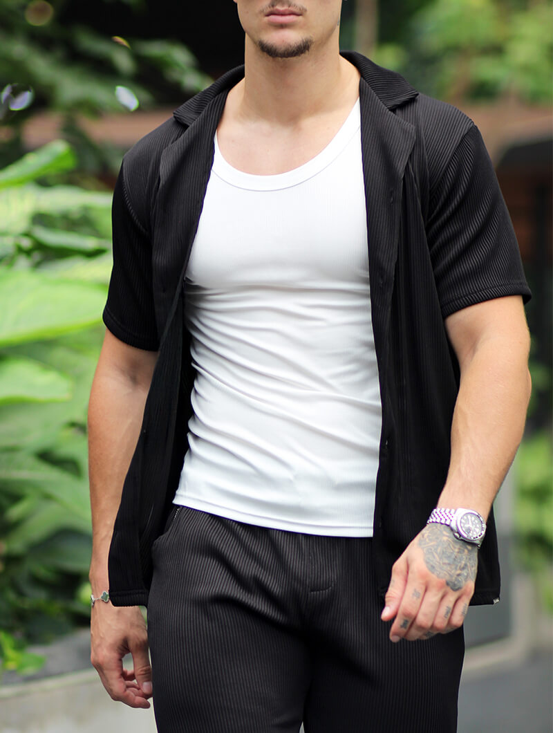 Man wearing a  Balinaro Bailey black  open shirt over a white t-shirt with black pants, standing outdoors.